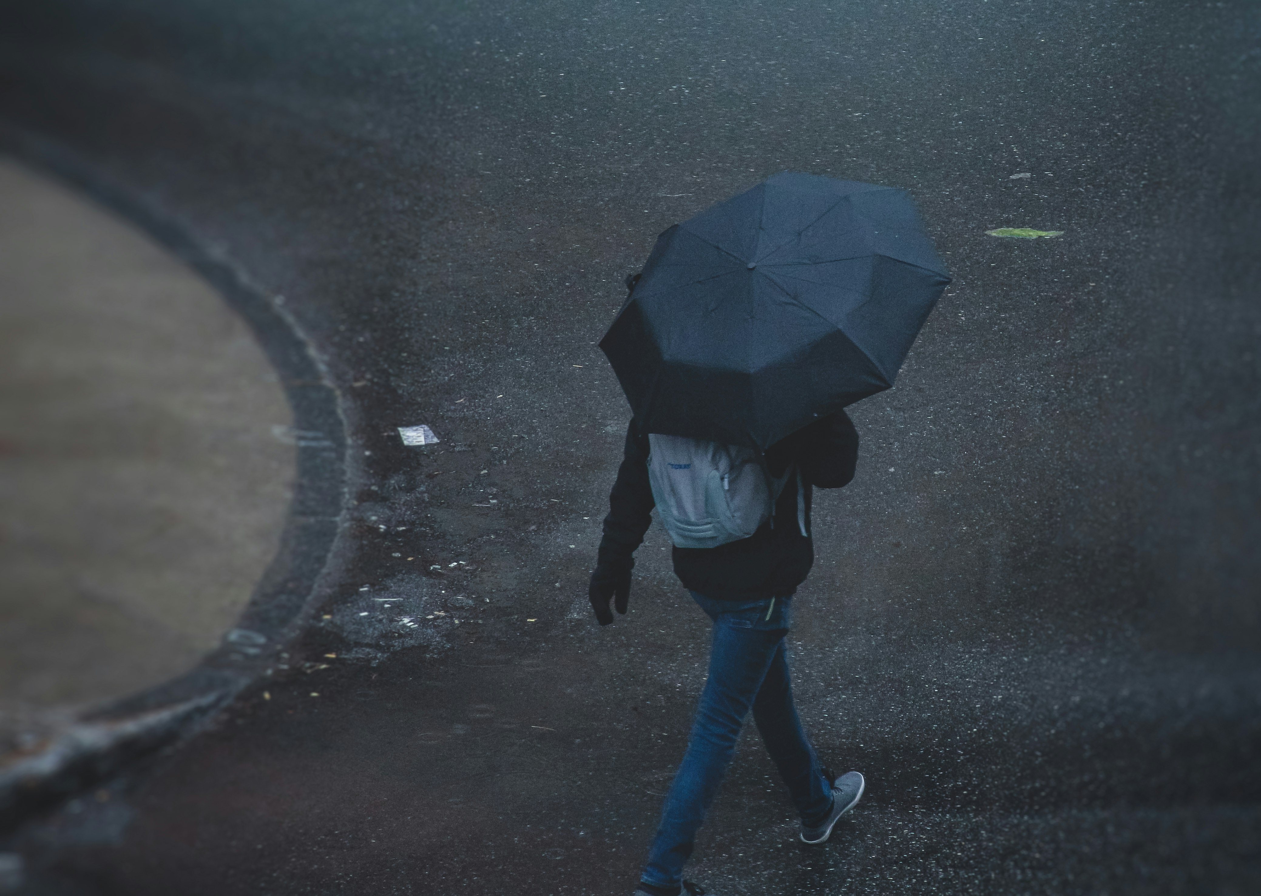 person in black jacket and blue denim jeans walking on wet road